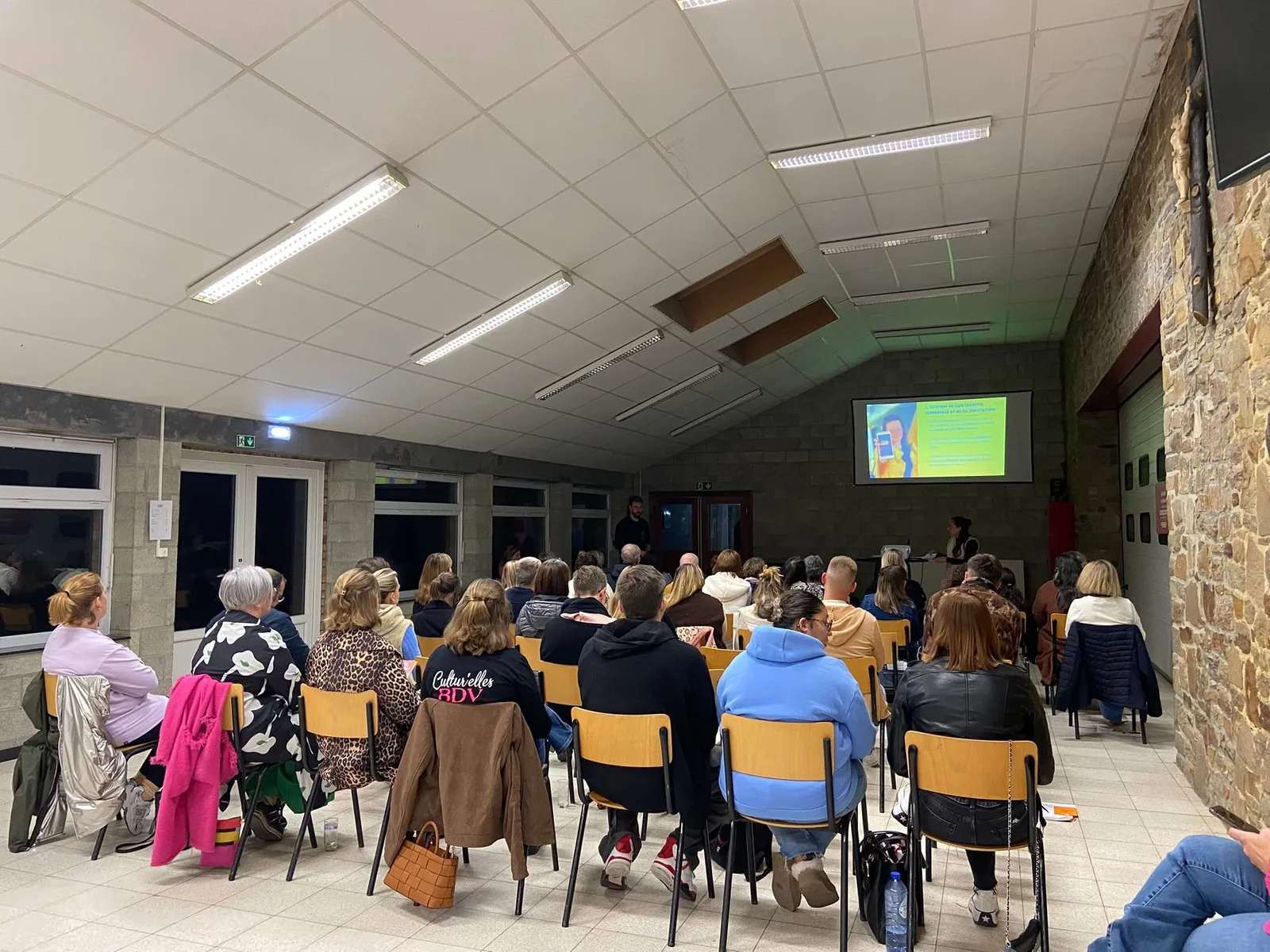 Une salle remplie de personnes assises face à un écran, pendant une séance d'information sur les jeunes et les réseaux sociaux