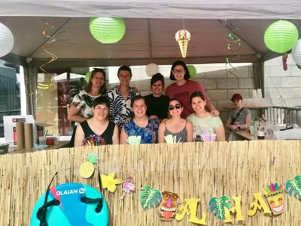 L'équipe derrière le bar décoré de lampions et de lettres « Aloha », à la fancy fair de l'école en juin 2025